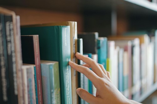 A hand reaching for a book on a shelf filled with various colorful books.