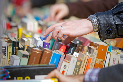 A hand reaches for a book among a colorful display of various books on a table.