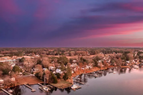 Aerial view of a serene lakeside community at sunset, with colorful skies and boats docked along the shore.