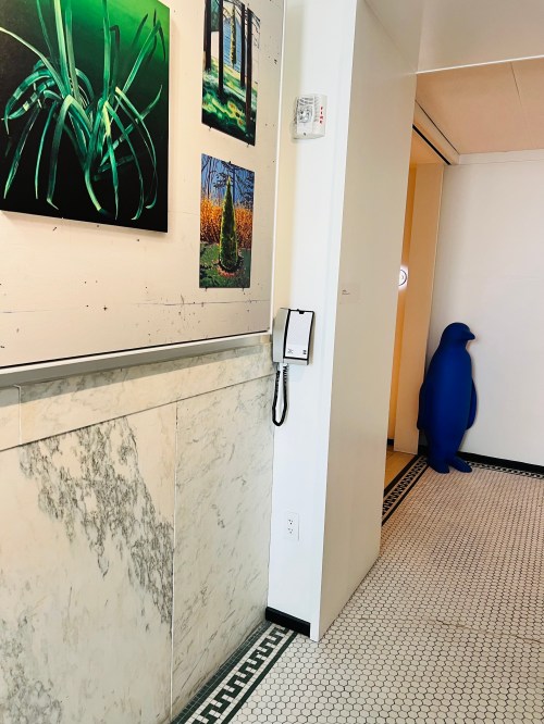 A hallway with green artwork on the wall, a marble panel, and a blue penguin sculpture in the corner.