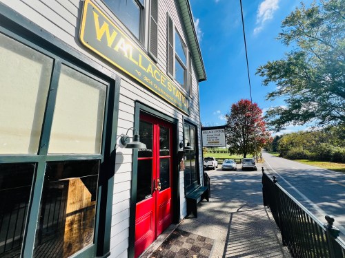 Exterior view of the Wallace Station building, featuring a red door and a sign, with trees and a road in the background.