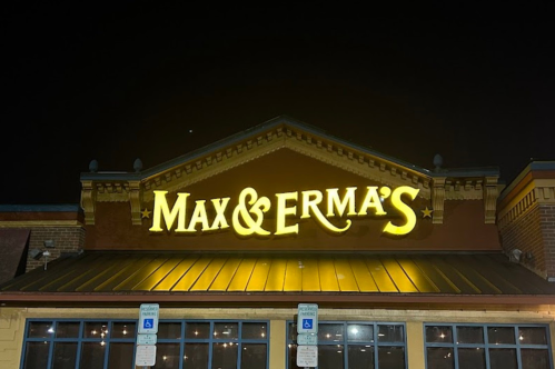Sign for Max & Erma's restaurant illuminated at night, featuring a decorative roof and parking signs below.