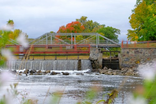 A small dam with a waterfall, surrounded by colorful autumn trees and a calm river.