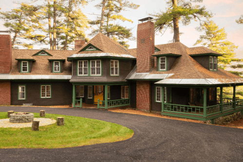 The lodge at Quietude conference center in Tuftonboro, New Hampshire. A firepit sits in the forefront. The lodge is set against a backdrop of trees.