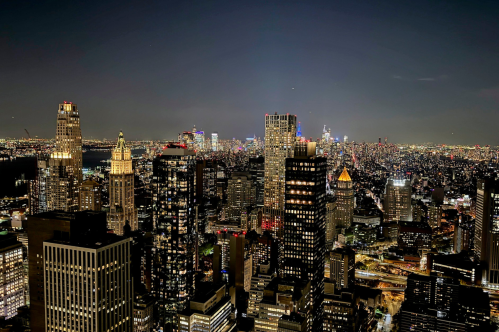 A panoramic view of a vibrant city skyline at night, illuminated buildings, and distant lights stretching across the horizon.