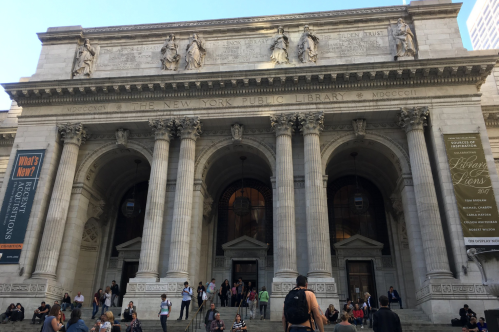 The New York Public Library's grand entrance features large columns and sculptures, with people walking up the steps.