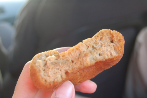 A hand holding a partially bitten, golden-brown chicken nugget with a soft, textured interior.