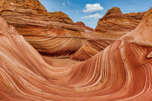 Colorful, undulating rock formations with layered textures in a desert landscape under a blue sky.