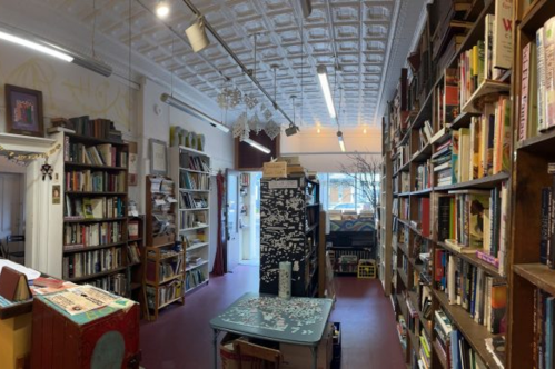 The interior of Volume Two: A Never Ending Books Collective in New Haven, CT. There are many shelves of books and a small table with a puzzle on it.