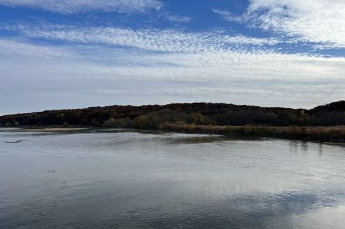 A serene river scene with a cloudy sky and autumn-colored trees lining the shore.