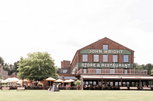 A brick building with "John Wright Store & Restaurant" signage, surrounded by outdoor seating and greenery.