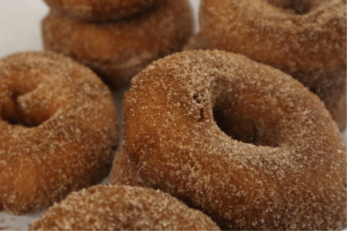 A close-up of freshly made, cinnamon-sugar coated donuts stacked on a plate.