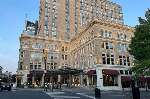 Historic hotel building with modern tower, featuring large windows and a canopy entrance, set in an urban environment.