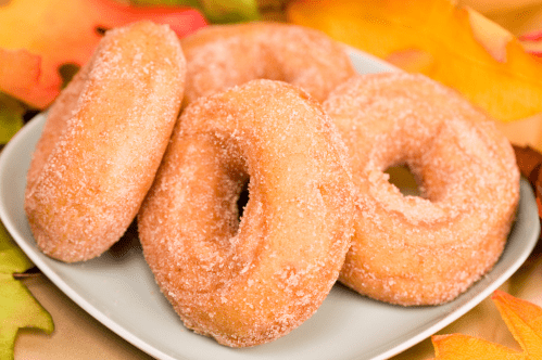 A plate of sugar-coated donuts surrounded by colorful autumn leaves.