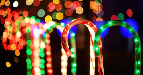 Colorful candy canes are lit up at night. Colorful lights are visible in the background.