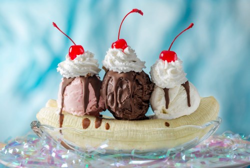 A banana split with three scoops of ice cream topped with whipped cream and cherries, served in a glass dish.