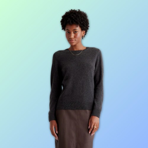 A woman with curly hair wearing a dark sweater and a skirt, standing against a gradient background.