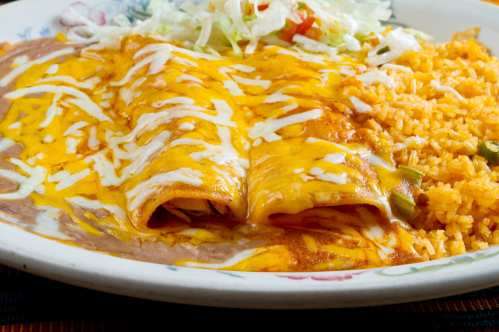 A plate of enchiladas topped with cheese and sauce, served with rice and a side of shredded lettuce.