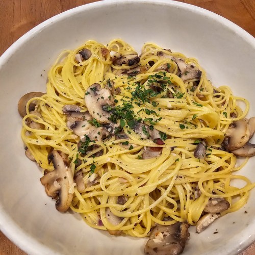 A bowl of spaghetti with sautéed mushrooms and herbs, garnished with parsley on a wooden table.