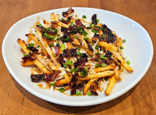 A plate of crispy fries topped with chopped bacon and green onions on a wooden table.