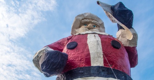 A towering Santa Claus statue in North Pole, Alaska, holding a scroll against a blue, cloudy sky.