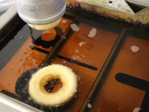 A donut frying in hot oil, with bubbles forming around it in a deep fryer.