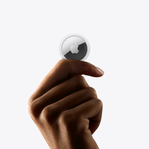 A hand holding an Apple AirTag against a plain white background.