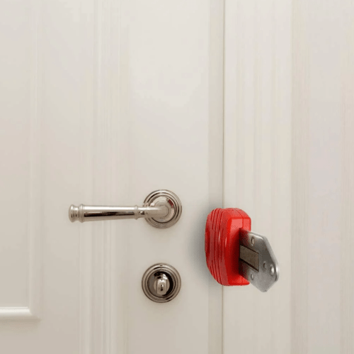 A red padlock secured on a white door handle, preventing access.