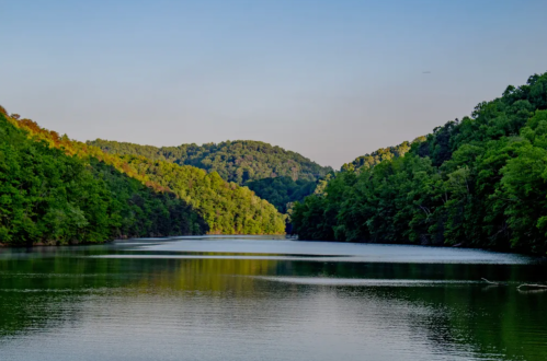 A serene lake surrounded by lush green hills under a clear sky, reflecting the landscape in calm waters.