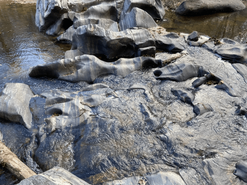 Smooth, dark rocks partially submerged in a shallow stream, with water flowing over and around them.