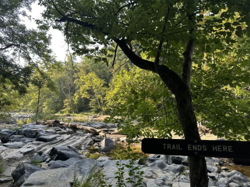 A serene river scene with rocks and trees, featuring a sign that reads "Trail Ends Here."