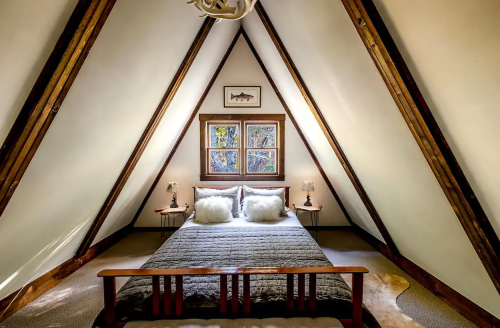 Cozy A-frame bedroom with a double bed, wooden accents, and large windows letting in natural light.