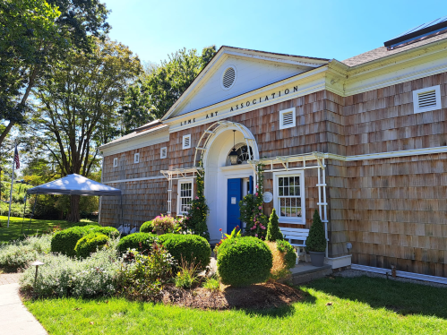 A charming wooden building with a blue door, surrounded by greenery and a tent, labeled "Link Art Association."