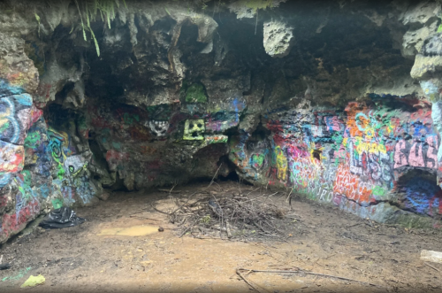 A colorful, graffiti-covered cave interior with a small pile of sticks on the ground.