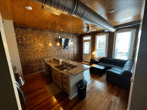 Cozy kitchen and living area with exposed brick walls, wooden ceiling, and modern furnishings.