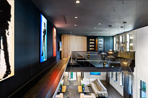 Modern interior with a balcony, featuring artwork on black walls, stylish lighting, and a cozy living area below.
