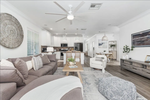 A modern living room with a sectional sofa, coffee table, and open kitchen in the background, featuring light decor.