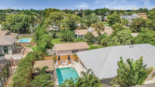 Aerial view of a lush backyard with a pool, surrounded by greenery and residential homes under a clear blue sky.