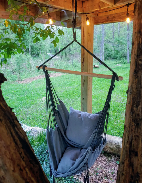 A cozy hammock chair hangs under a wooden structure, surrounded by greenery and soft glowing lights.