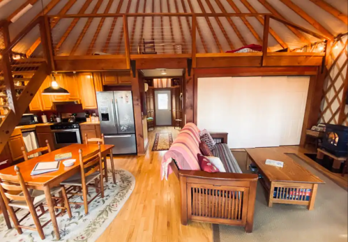 Cozy interior of a wooden cabin with a kitchen, dining area, and living space featuring a sofa and coffee table.