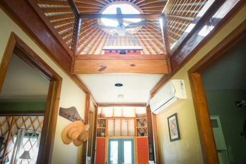 Interior view of a home featuring a wooden balcony, ceiling fan, and bright natural light streaming through windows.