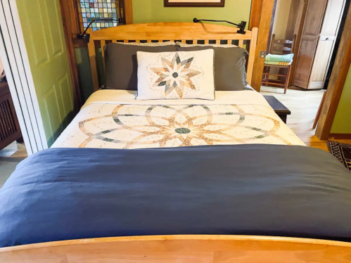 A cozy bedroom featuring a wooden bed with a decorative quilt and a pillow, set in a warm, inviting space.