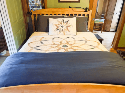 A cozy bedroom featuring a wooden bed with a decorative quilt and a pillow, set in a warm, inviting space.