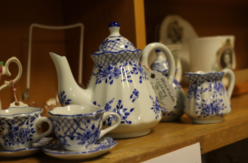 A decorative blue and white porcelain tea set, including a teapot, creamer, and cups, displayed on a wooden shelf.