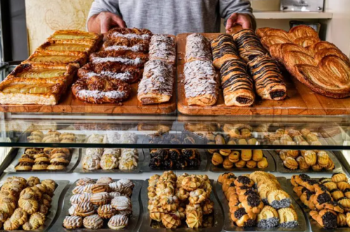 A display of various pastries and baked goods, including croissants, danishes, and cookies, on wooden trays.