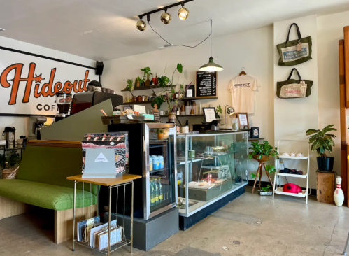 Cozy coffee shop interior with a green seating area, display case, plants, and a welcoming atmosphere.