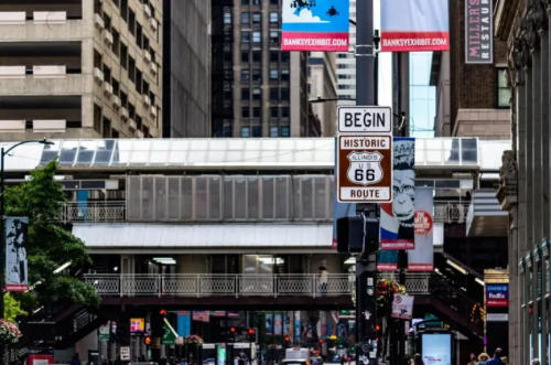 Street view featuring a "Historic Route 66" sign, with buildings and banners in a bustling urban setting.