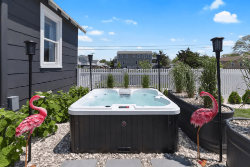 A hot tub surrounded by greenery and flamingo decorations, with a clear blue sky in the background.