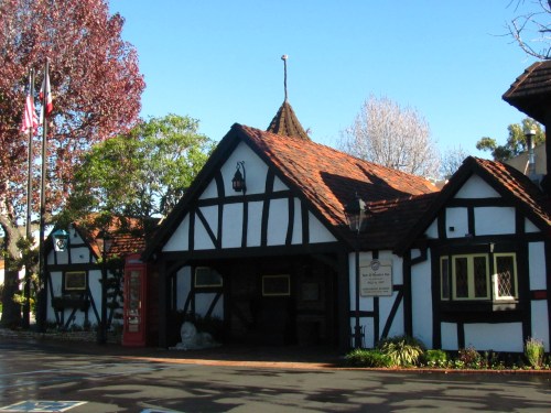 A charming Tudor-style building with a red roof, surrounded by trees and clear blue skies.