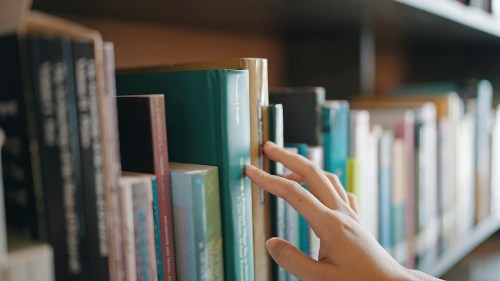 A hand reaching for a book on a shelf filled with various colorful books.
